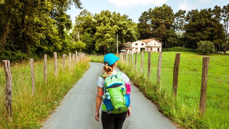 Woman walking on the Camino de Santiago in Spain near a farmhouse.