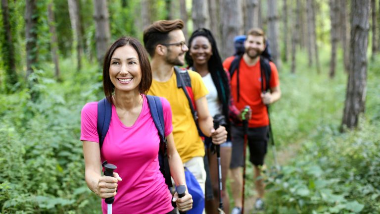 Group of friends hiking for health with polls in the forest.
